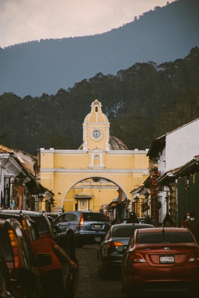 pexels-photo-13399865-13399865 Scenic view of Santa Catalina Arch in Antigua Guatemala with vehicles and mountain backdrop.